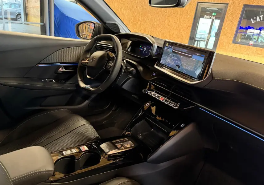 Vue intérieure côté conducteur du Peugeot 208 blanc 1.2 Hybrid 136 GT, mettant en valeur le tableau de bord numérique et l'écran tactile central.