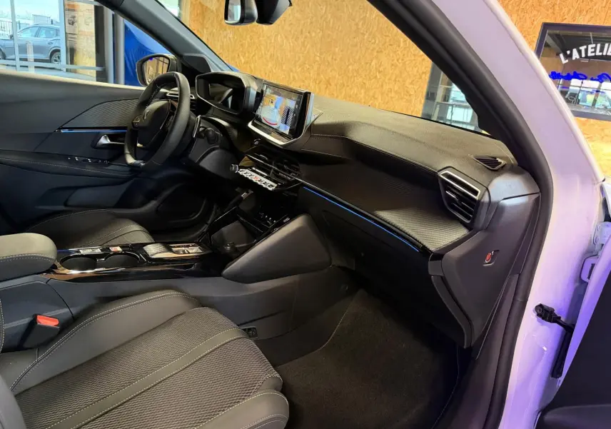Vue intérieure côté passager de la Peugeot 208 1.2 Hybrid 136 GT blanche, avec tableau de bord noir et écran tactile allumé.