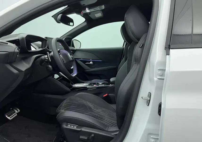 Vue intérieure côté conducteur d'une Peugeot 208 blanche, sièges sport noirs avec surpiqûres et volant multifonction.