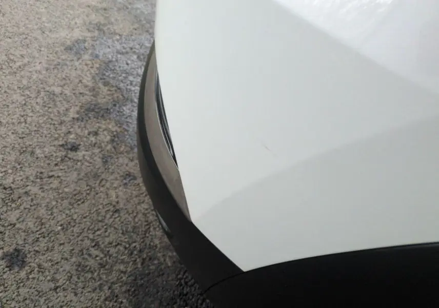 Gros plan sur l'angle avant droit blanc du Renault Captur 2024 avec pare-chocs noir et surface lisse.