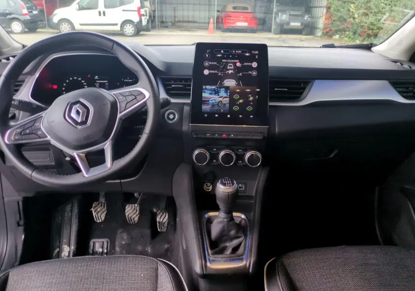 Vue intérieure avant du Renault Captur blanc 2024, volant multifonction, écran tactile vertical et levier de vitesse manuel.