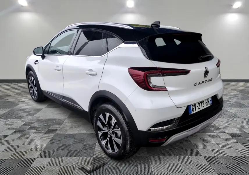 Vue 3/4 arrière droite du Renault Captur blanc avec toit noir et jantes alliage bicolores sur fond neutre.