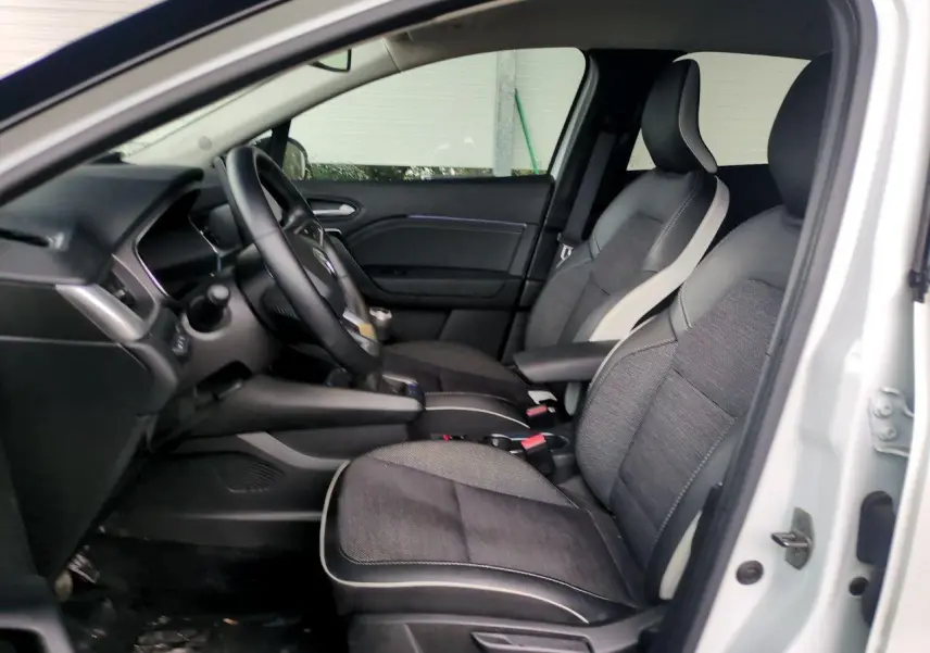 Vue intérieure côté conducteur du Renault Captur blanc 2024, sièges bi-matière gris et noir avec accoudoir central.