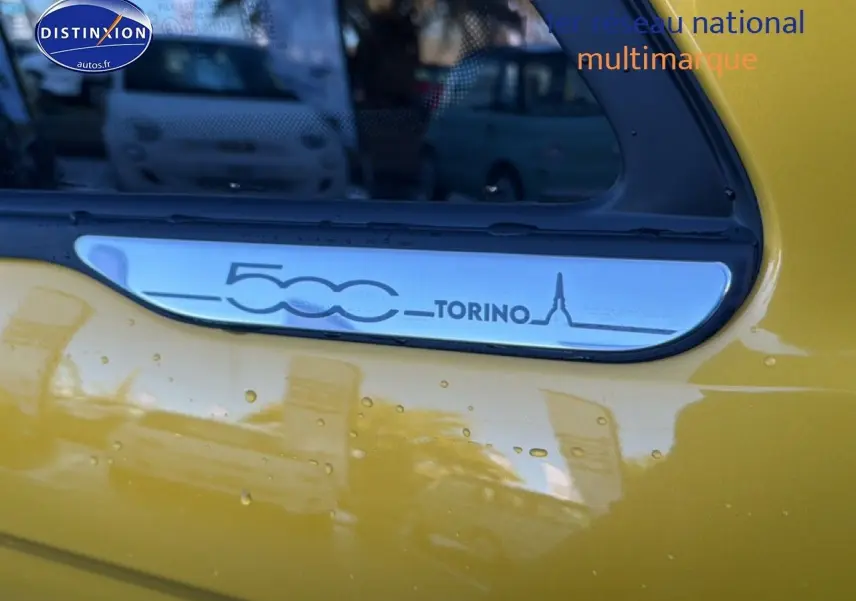 Détail du logo 500 Torino sur la portière jaune gold métal d'une Fiat 500 hybride.