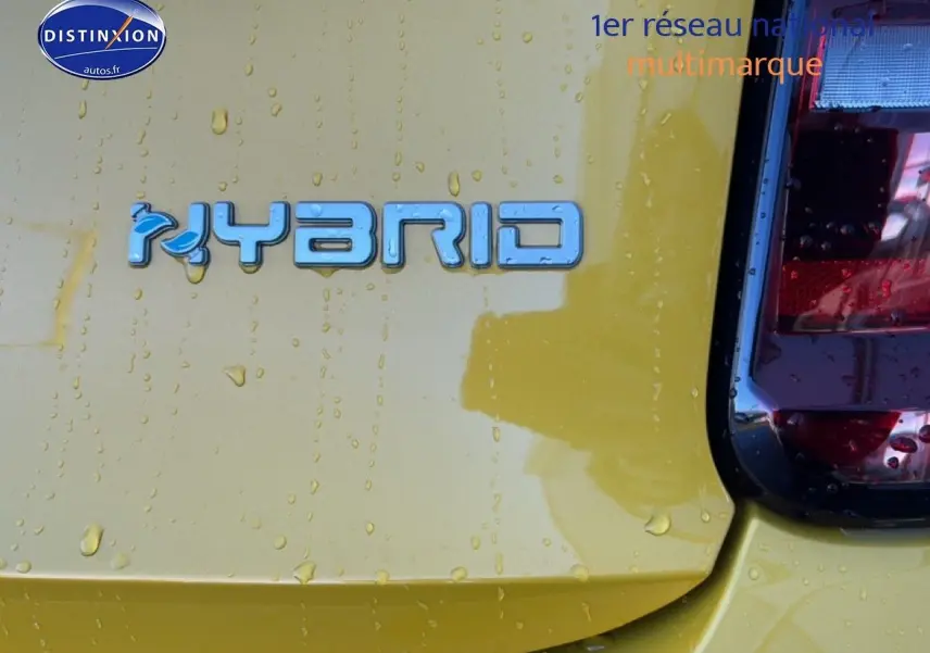 Gros plan sur le logo Hybrid bleu sur la partie arrière droite d'une FIAT 500 Yellow Gold Métal avec gouttes d'eau visibles.