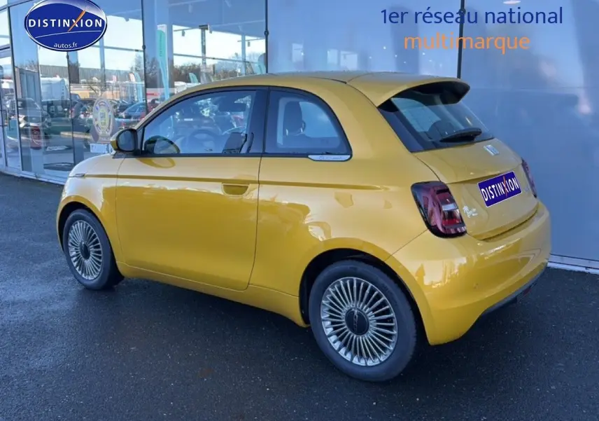 Vue 3/4 arrière droite d'une FIAT 500 Yellow Gold Métal avec jantes alu et becquet arrière, stationnée devant une vitrine.