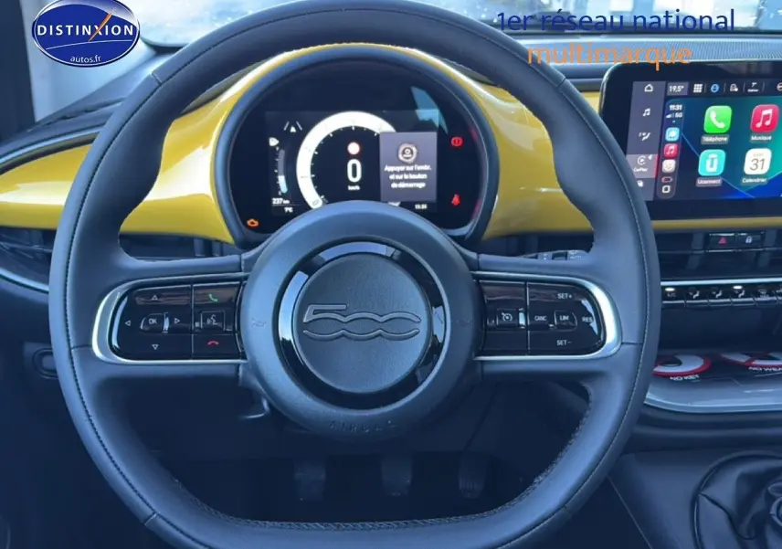 Vue centrée sur le volant noir et tableau de bord jaune or métallisé de la Fiat 500 hybrid avec écran tactile multifonction.