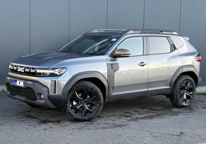 Dacia Duster 2026 gris schiste en vue 3/4 avant droit, avec jantes alliage noires et barres de toit longitudinales.