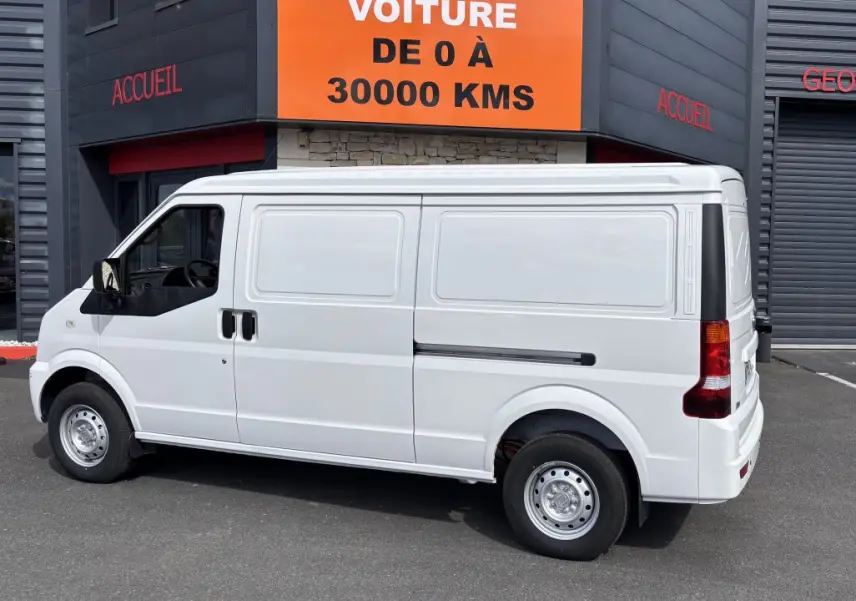 Vue de profil côté gauche du fourgon électrique blanc DFSK EC35 BEV 39KWH, stationné devant un bâtiment commercial.