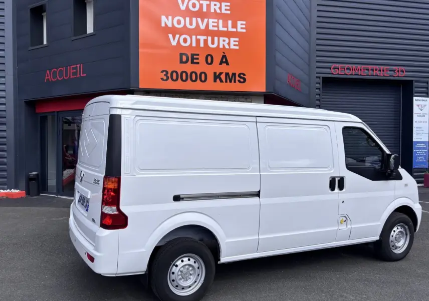 Vue 3/4 arrière droite d'un utilitaire blanc DFSK EC35 électrique stationné devant un bâtiment commercial.