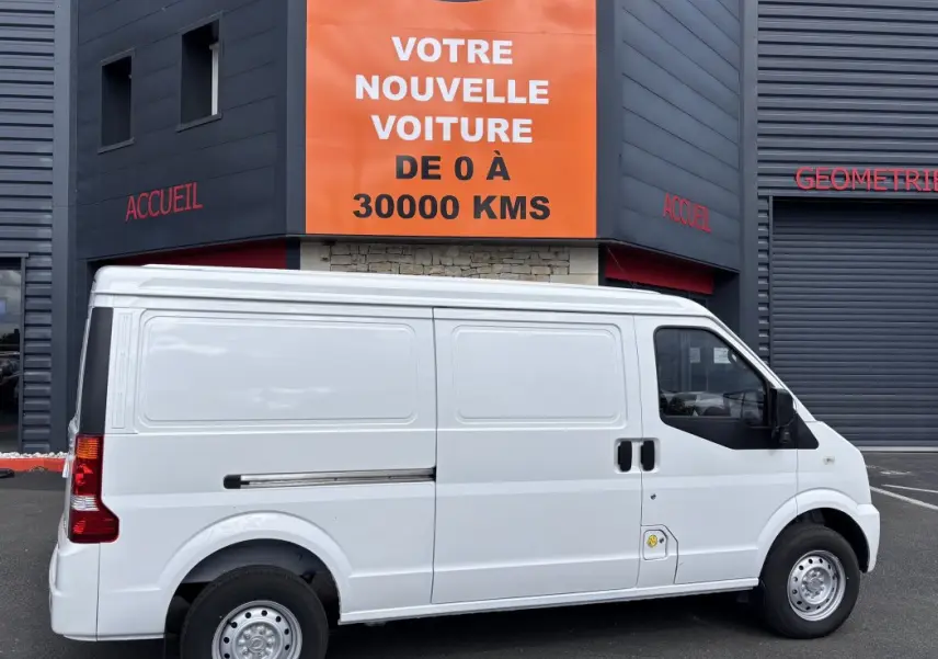 Vue latérale droite d'un utilitaire blanc DFSK EC35 électrique stationné devant un bâtiment commercial.