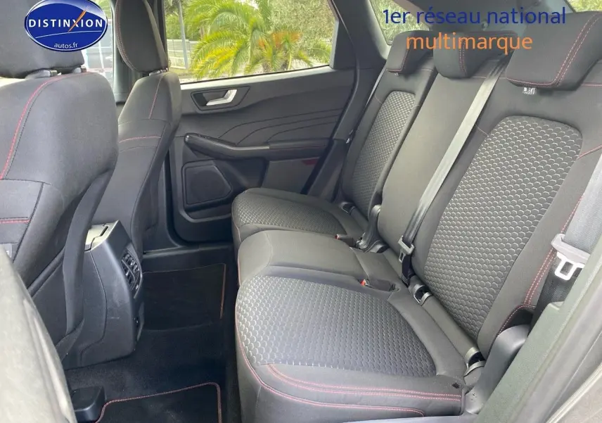 Vue intérieure arrière droite du Ford Kuga 2025, montrant la banquette tissu gris avec surpiqûres rouges et portes ouvertes.