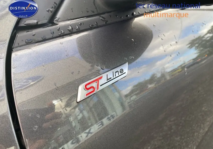 Gros plan sur l'écusson ST-Line rouge et argent sur la porte côté gauche d'un Ford Kuga gris métallisé avec gouttes d'eau.