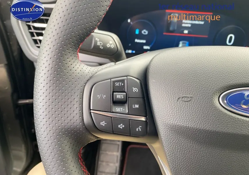 Gros plan sur le volant perforé avec surpiqûres rouges du Ford Kuga 2025, boutons multifonctions visibles.