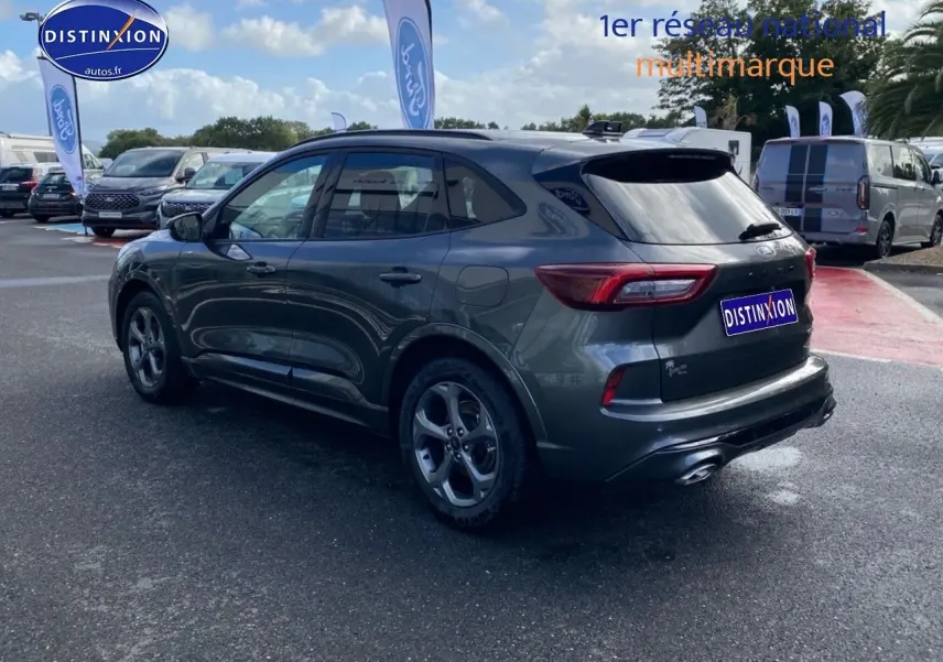 Ford Kuga gris métallisé vu en 3/4 arrière droit, avec jantes alu et feux arrière LED dans un parking extérieur.