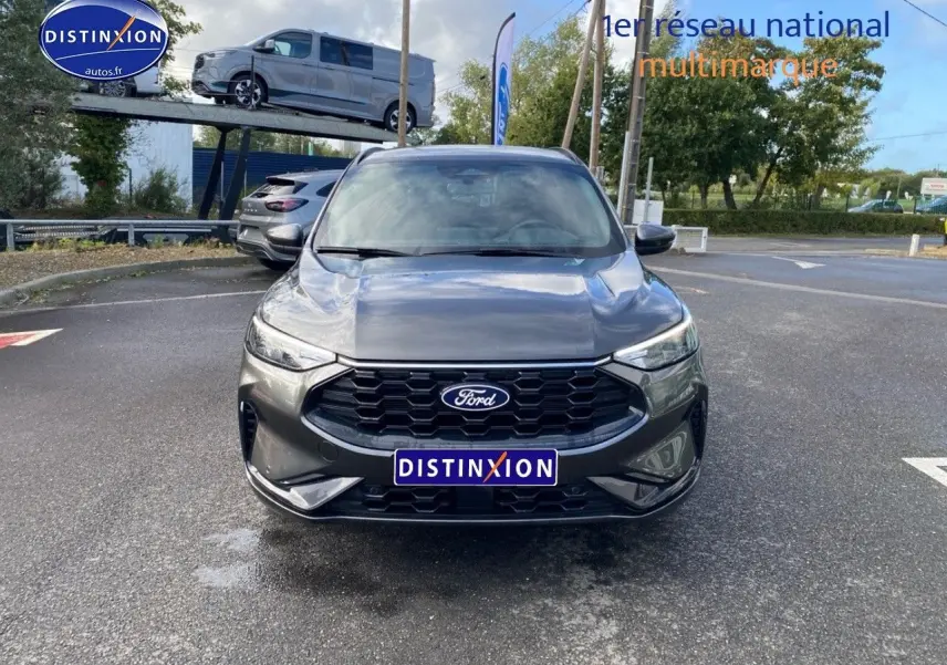 Vue avant d'un Ford Kuga gris métallisé avec calandre noire et phares LED, stationné sur un parking extérieur.