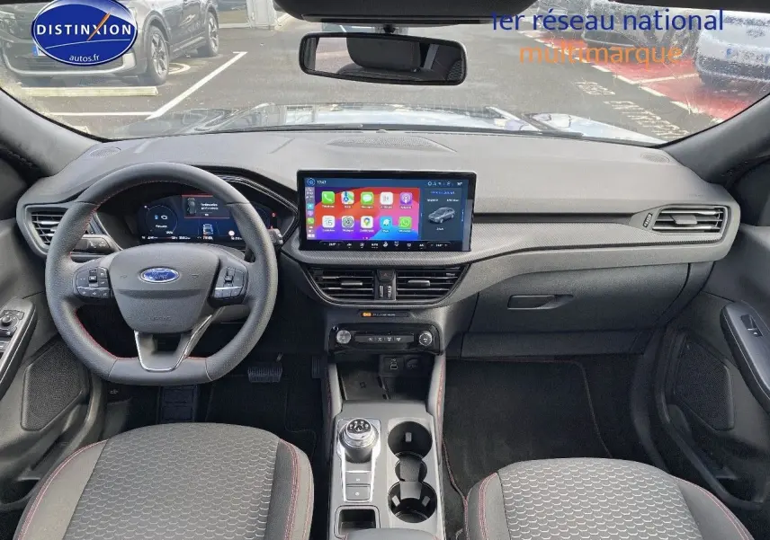 Vue intérieure avant du Ford Kuga 2025 avec tableau de bord moderne, écran tactile central et volant multifonction.