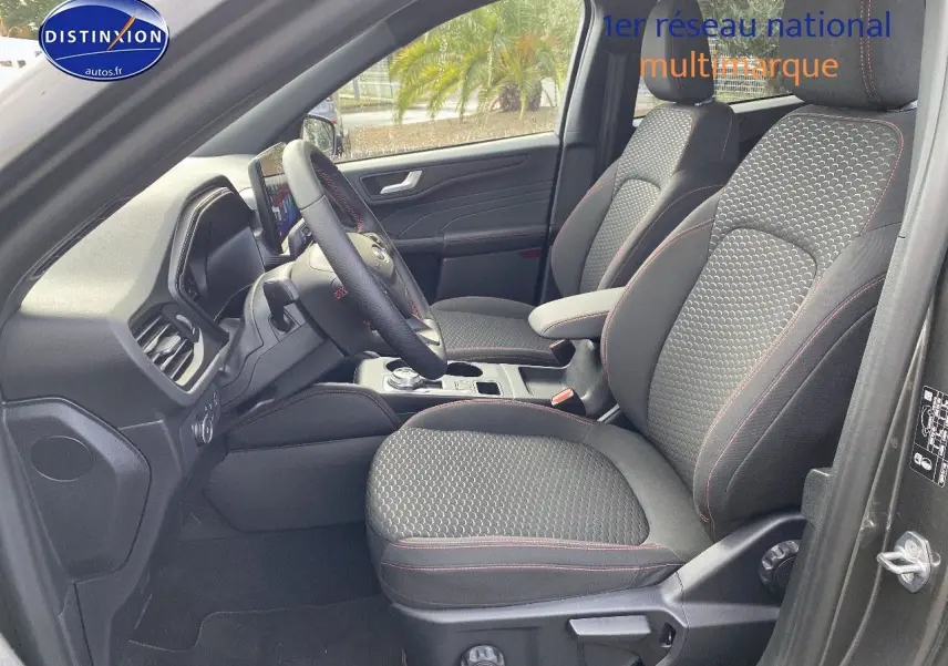 Vue intérieure côté conducteur du Ford Kuga 2025, sièges tissu gris avec surpiqûres rouges et volant multifonction.