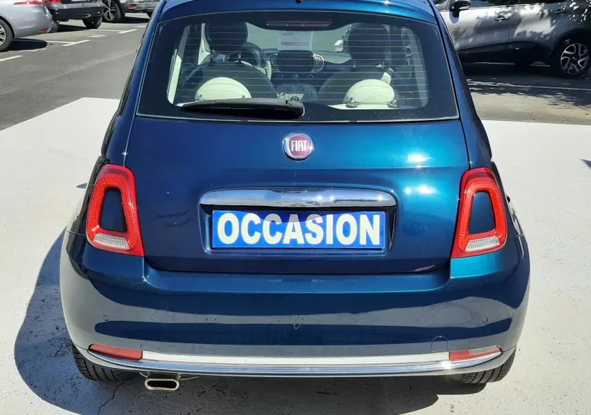 Vue arrière d'une FIAT 500 bleu métallisé avec plaque "OCCASION" sur un parking ensoleillé.