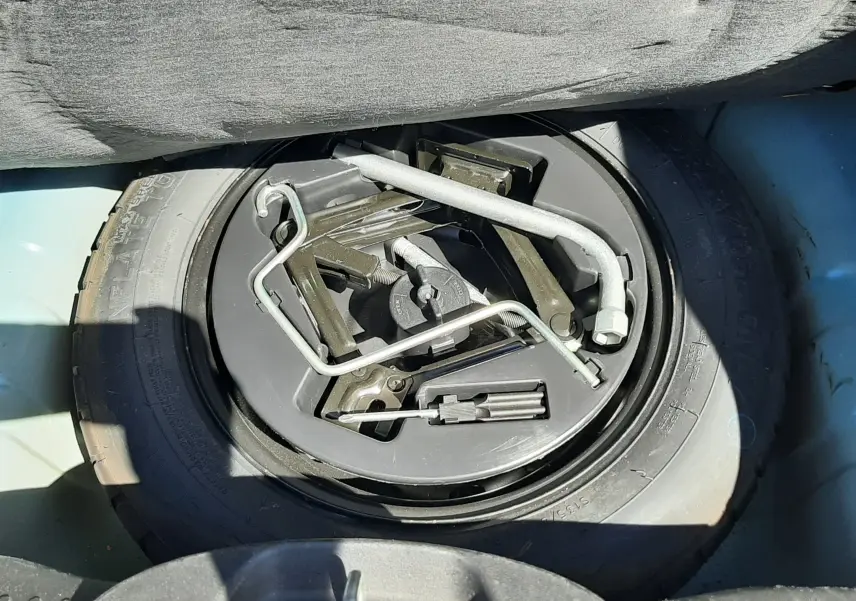 Vue plongeante sur la roue de secours et les outils de bord dans le coffre d'une FIAT 500 bleu 2018.