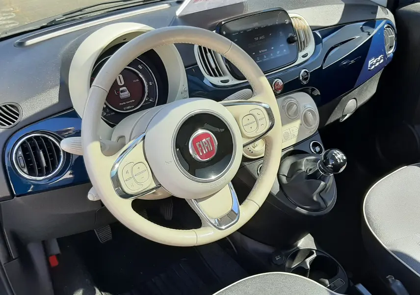 Vue intérieure côté conducteur de la FIAT 500 1.2 8V 69 Lounge 2018 avec tableau de bord bleu et volant beige.