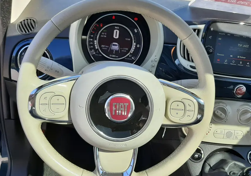 Vue rapprochée du volant beige clair de la Fiat 500 1.2 8V 69 Lounge 2018 avec tableau de bord numérique et console centrale.