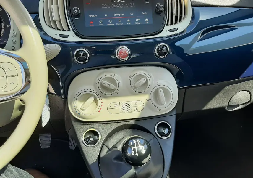 Vue intérieure centrée sur la console centrale et levier de vitesses manuelle d'une Fiat 500 bleu avec écran tactile et commandes de climatisation.