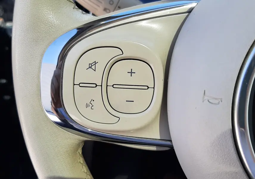 Gros plan sur les commandes de volume et de coupure du son sur le volant beige clair d'une Fiat 500 Lounge bleue de 2018.