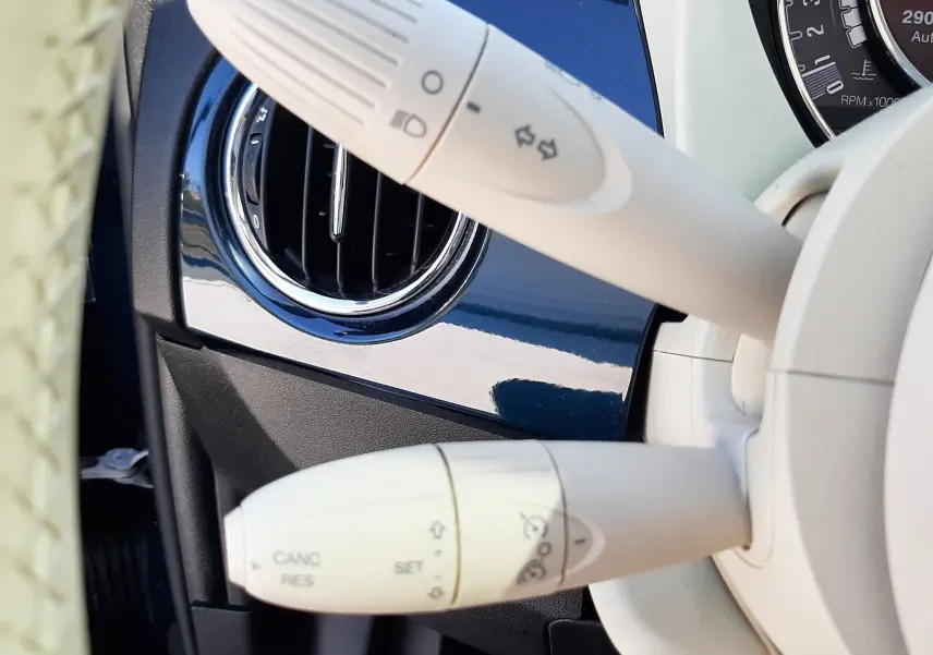 Détail intérieur montrant les commandes de clignotants et régulateur sur fond bleu brillant d'une Fiat 500 2018.