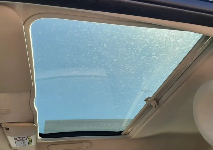 Toit ouvrant panoramique ouvert sur l'intérieur beige d'une FIAT 500 bleue, vue côté conducteur vers le ciel.