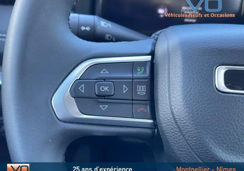 Gros plan sur les commandes gauche du volant noir du Jeep Compass blanc 2024 avec boutons multifonctions intégrés.