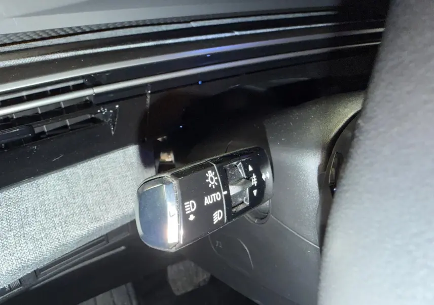 Gros plan sur la commande des phares à gauche du volant dans l’habitacle noir du Peugeot 3008 gris 2025.