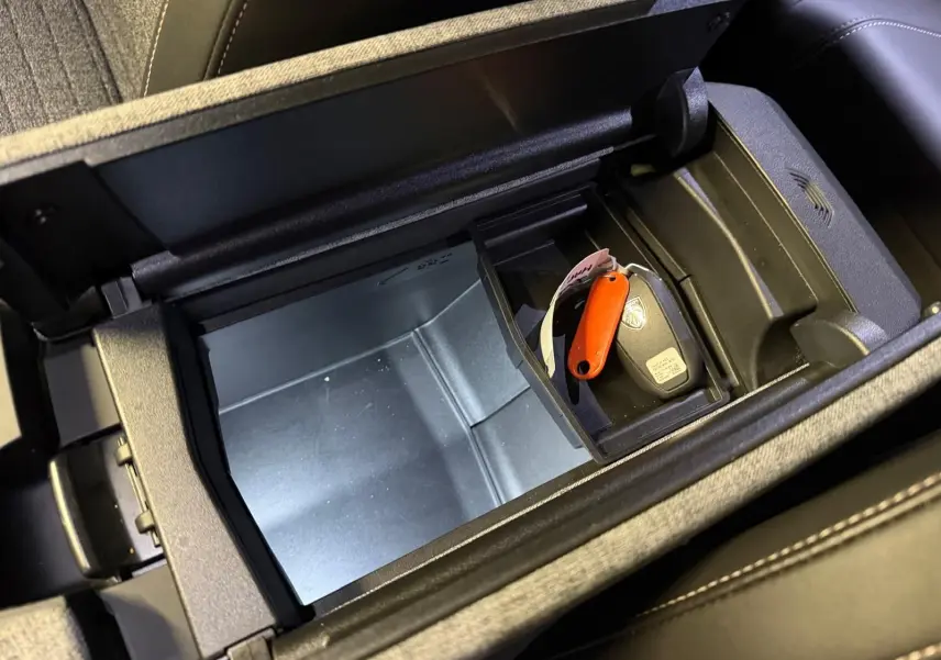 Vue plongeante sur le rangement central noir du Peugeot 3008 gris avec clé et porte-clés orange à l’intérieur.