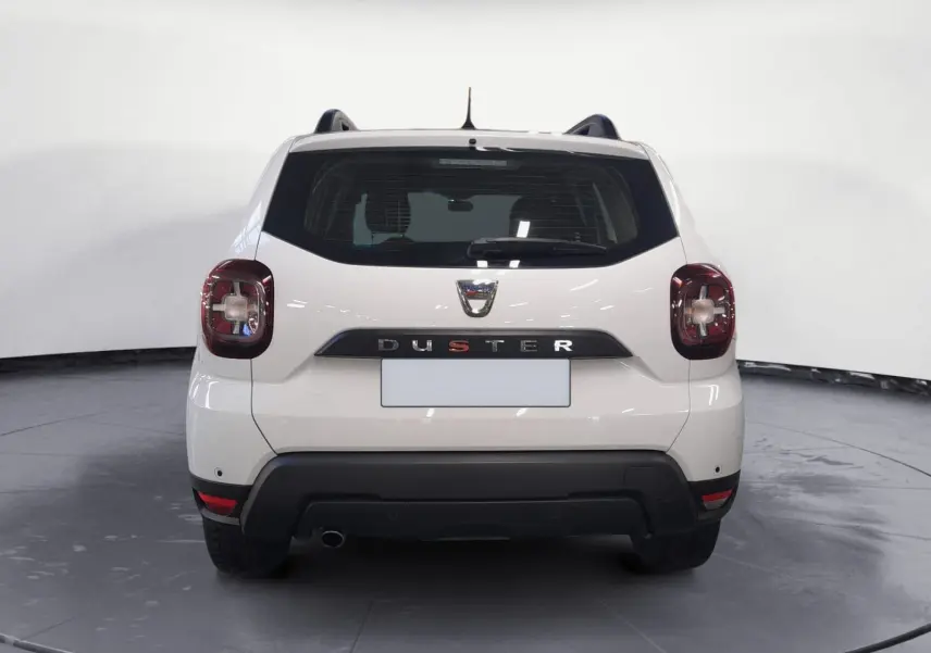 Vue 3/4 arrière droite d'un Dacia Duster blanc 2021 avec jantes alliage et grille de séparation visible à l'arrière.