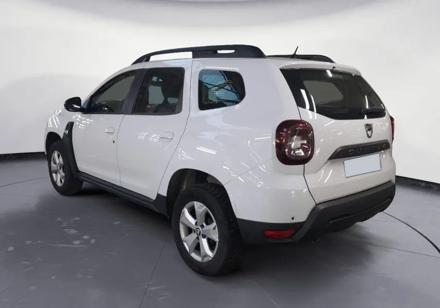 Profil côté gauche d’un Dacia Duster blanc 2021 avec jantes alliage et grille de séparation visible à l’arrière.