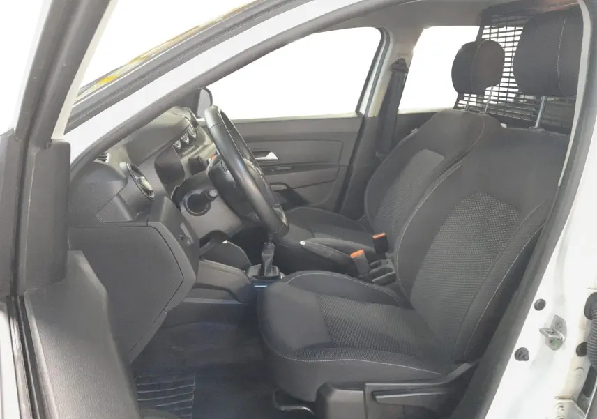 Vue intérieure côté conducteur du Dacia Duster blanc 2021, sièges noirs avec grille de séparation visible derrière.