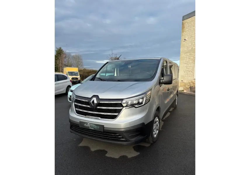 Renault Trafic Fourgon gris clair vu de face droite, avec calandre noire et phares LED distinctifs.