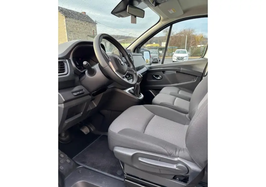 Vue intérieure côté conducteur du Renault Trafic Fourgon 2022, sièges gris et volant multifonctions visible.