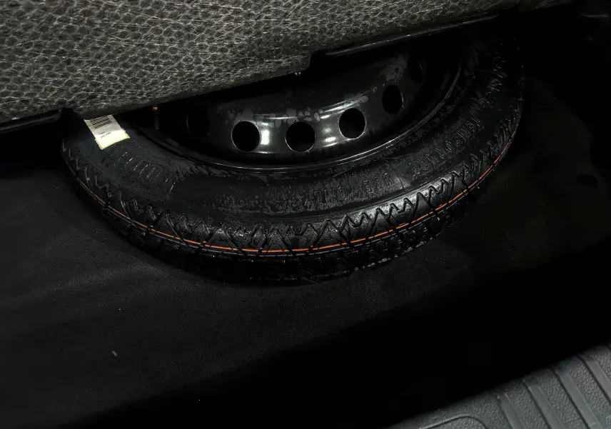 Gros plan sur la roue de secours noire en acier dans le coffre d'une Renault SYMBIOZ gris Cassiopé.