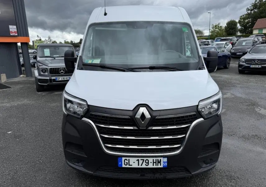 Renault Master blanc vu de face avec calandre noire et projecteurs antibrouillard sous un ciel nuageux.
