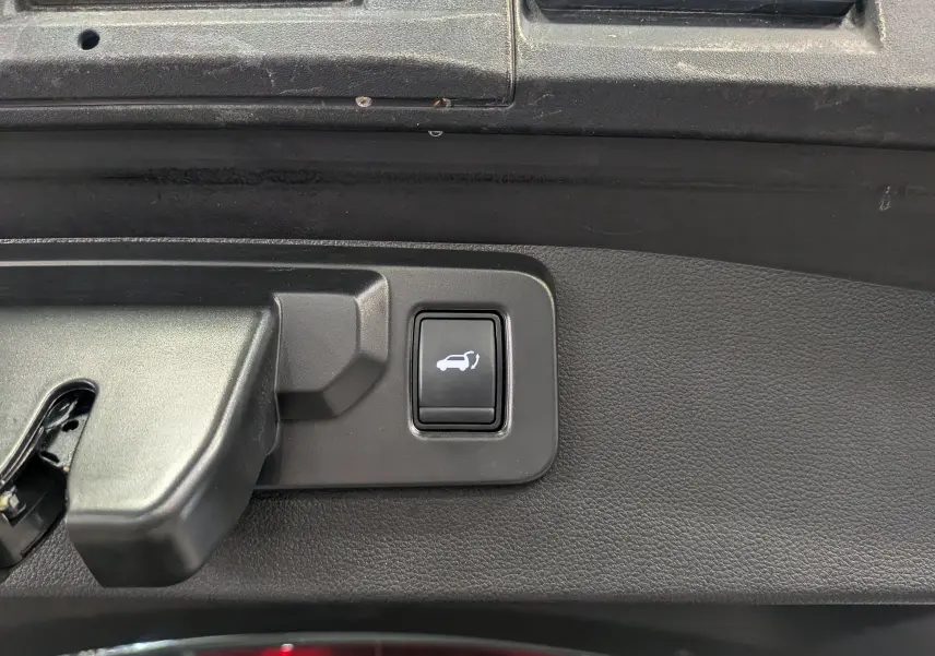 Bouton intérieur noir de commande d'ouverture du coffre sur Renault Symbioz E-TECH Gris Cassiopé, vue rapprochée.