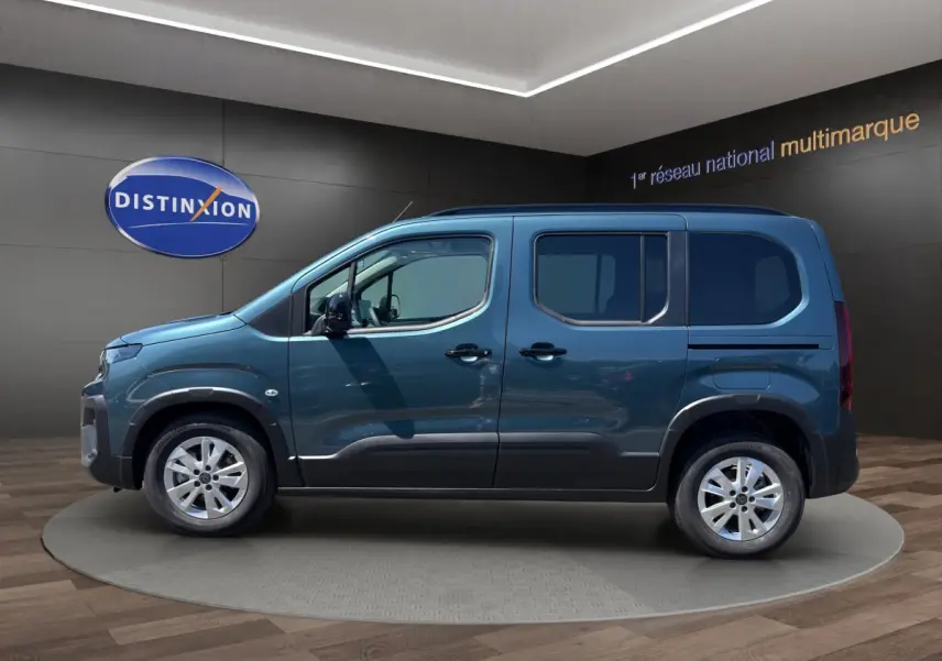 Vue de profil côté gauche du Peugeot Rifter bleu 2026 dans un showroom avec jantes argentées et portes coulissantes.