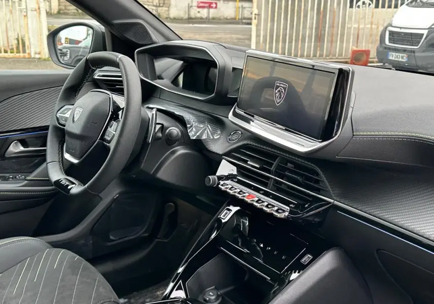 Vue intérieure côté conducteur du Peugeot 208 Hybrid 110 e-DCS6 GT 2025, avec volant compact, écran tactile et finitions noires.
