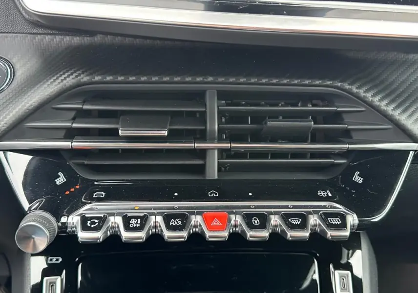 Détail du tableau de bord de la Peugeot 208 Hybrid 110 GT montrant les commandes de climatisation et les aérateurs noirs.