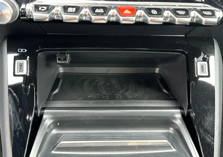 Vue rapprochée de la console centrale du Peugeot 208 gris, montrant le compartiment de recharge sans fil et les boutons de commande.