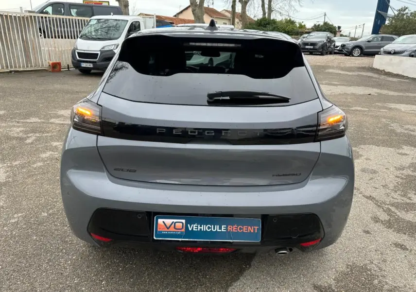 Vue arrière d'une Peugeot 208 gris 2025 avec feux arrière allumés et logo Peugeot en noir brillant.