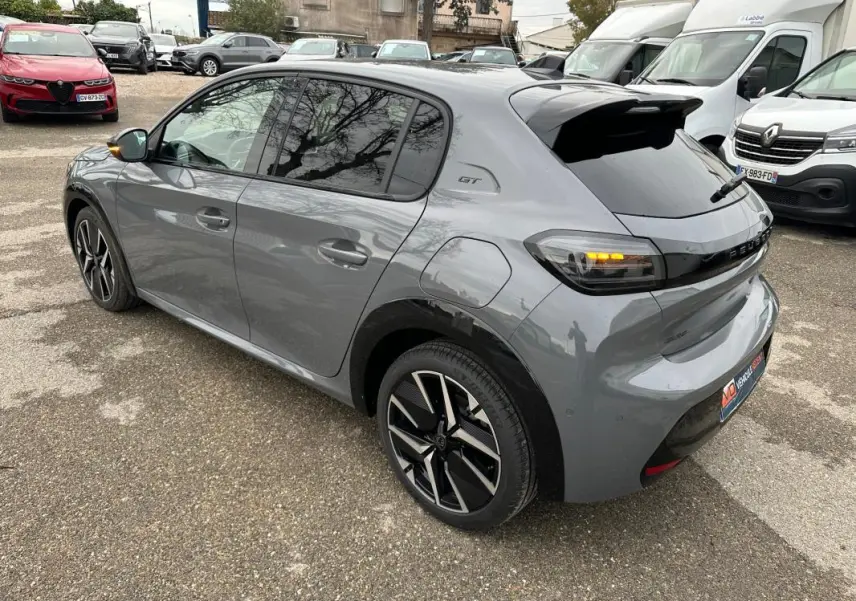 Vue 3/4 arrière droite d’une Peugeot 208 Hybrid 110 gris métallisé avec jantes alliage 17 pouces et feux arrière allumés.