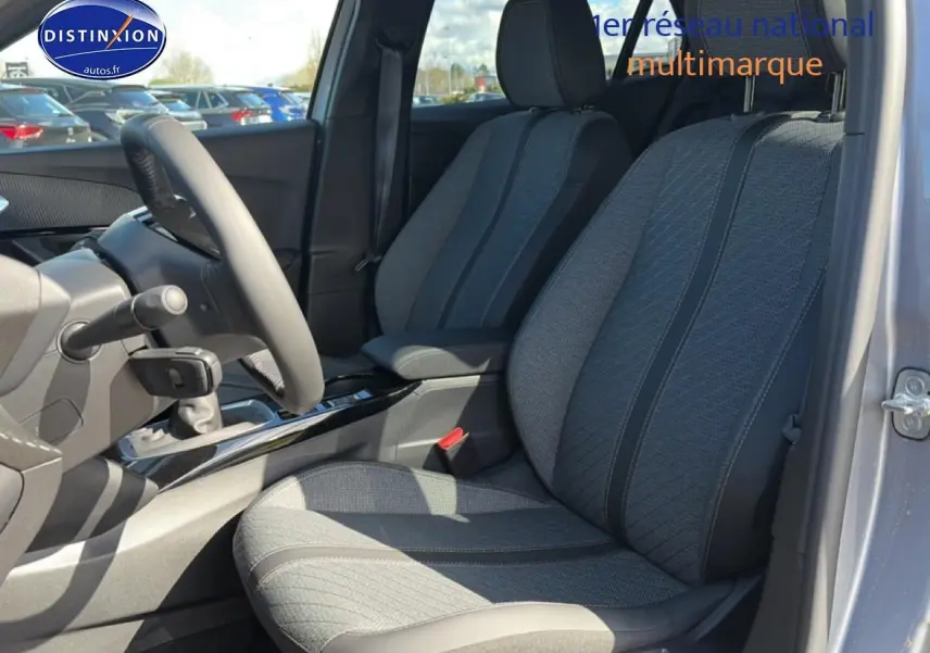 Vue intérieure côté conducteur du Peugeot 2008 1.2 100 allure gris artense, mettant en valeur les sièges tissu et la console centrale.