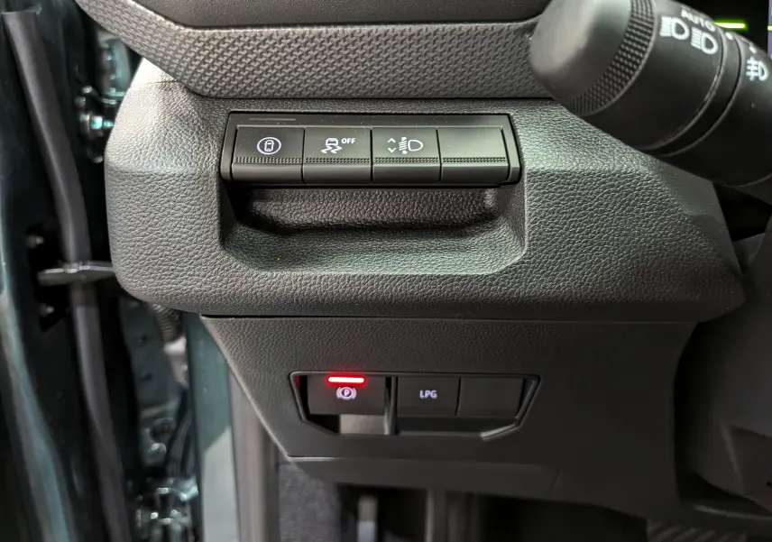 Gros plan sur les commandes noires du tableau de bord du Dacia Duster Hybrid-G 150 CH 4x4 en Vert Cèdre, avec bouton frein à main électronique allumé.