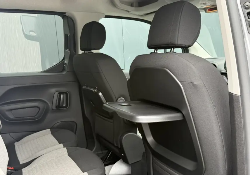 Vue intérieure arrière droite du Citroën Berlingo Multispace gris acier, montrant les sièges avec tablette rabattable intégrée.